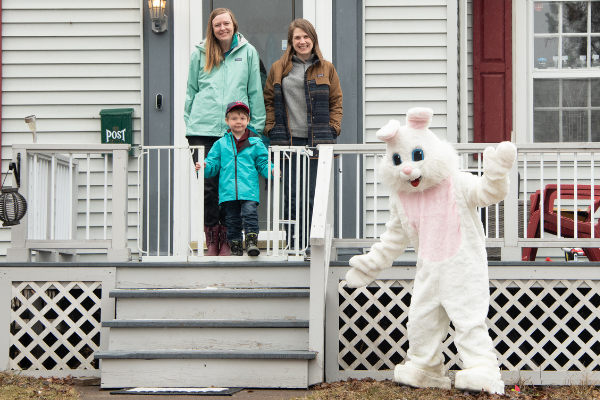 person in an Easter Bunny Costume posing in front of a house with two moms and a son