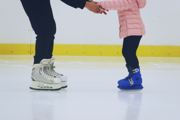 An adult helping a small child ice skate on an indoor rink with hockey skates